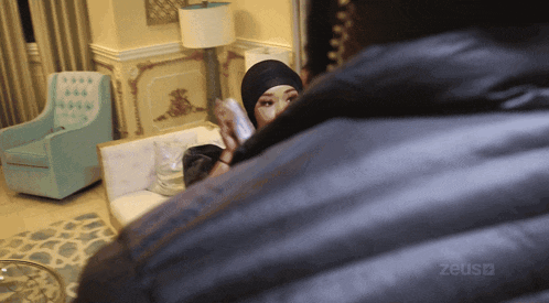 a woman in a hijab is talking on a cell phone in a room with a zeus logo