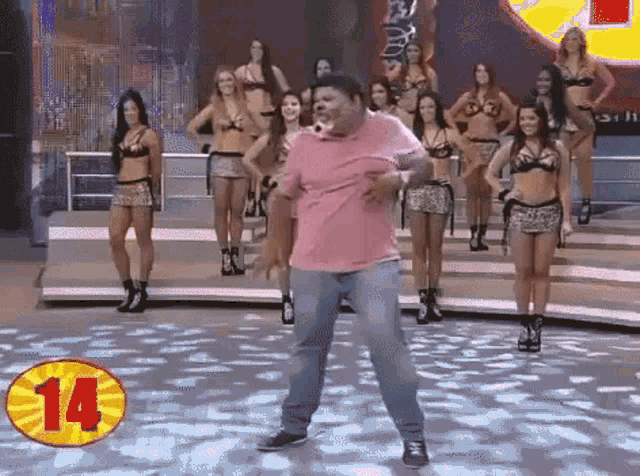a man in a pink shirt is dancing in front of a group of women in bikinis and the number 14 is visible