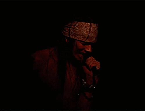 a shirtless man singing into a microphone with a headband on his head
