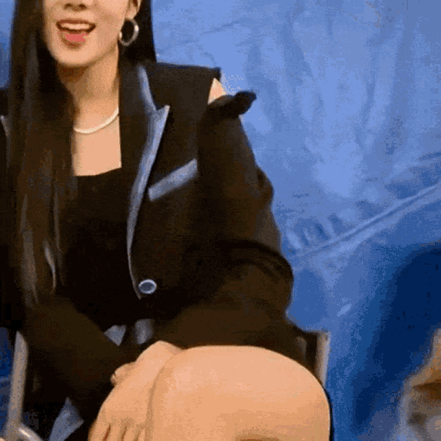 a woman in a black jacket is sitting in front of a blue backdrop