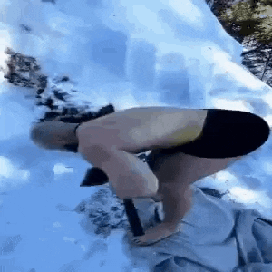 a man without a shirt is kneeling down in the snow with a hammer .