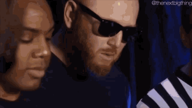 a man with a beard and sunglasses is standing next to a woman in a striped shirt .