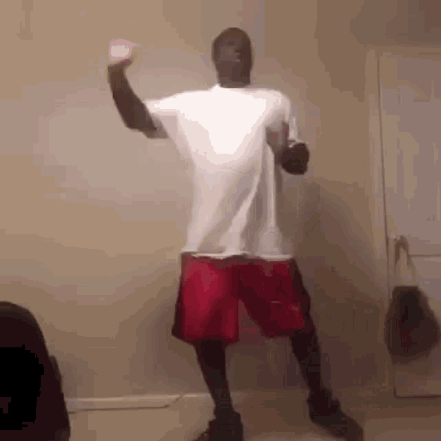 a man in a white shirt and red shorts is standing in a room .