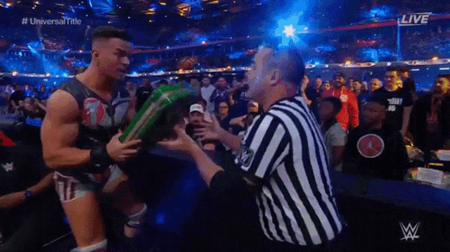 a referee in a striped uniform is talking to a wrestler who is holding a green object