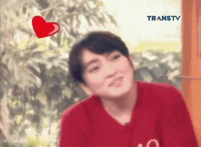 a young man in a red shirt is smiling with a red heart flying over his head .