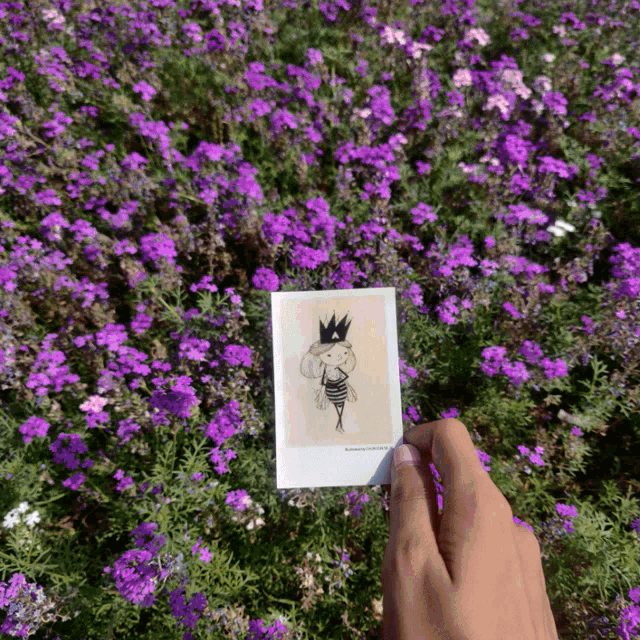 a person is holding a picture of a girl wearing a crown in front of purple flowers