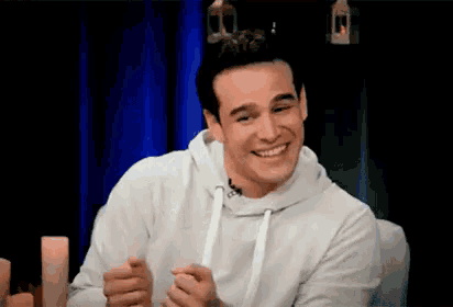 a man in a white hoodie is smiling while sitting on a couch .