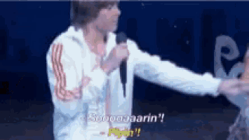 a man in a white jacket is holding a microphone and talking into it