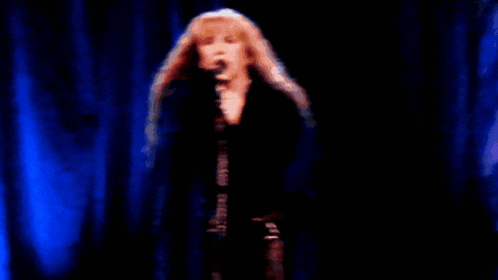 a woman singing into a microphone with a blue curtain in the background