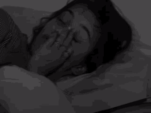 a woman is laying in bed with her hand on her face