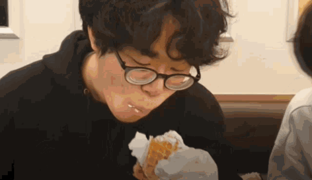 a young man wearing glasses is eating a waffle cone