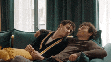 two men are laying on a blue couch and hugging each other
