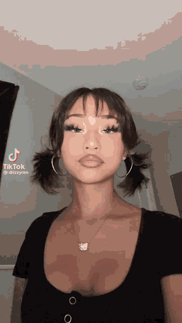 a woman with pigtails and hoop earrings is wearing a black top and necklace .
