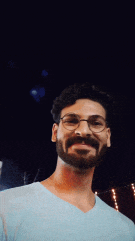 a man with glasses and a beard is smiling in front of a fireworks display