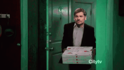 a man in a suit is holding a stack of pizza boxes in front of a green door .