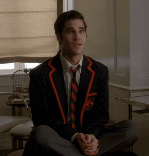 a man in a suit and tie sits on the floor with his legs crossed