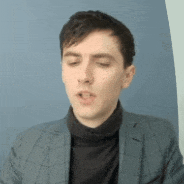 a young man wearing a suit and turtleneck is making a funny face .