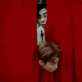 a couple of men are peeking out from behind a red curtain .