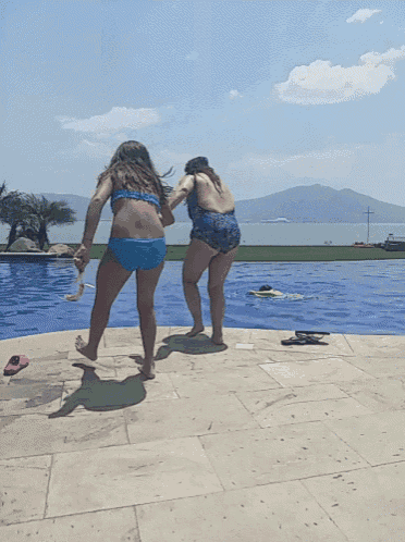 two women in bikinis are standing on the edge of a pool