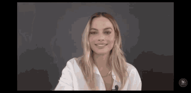 a woman in a white shirt with a microphone on her neck smiles
