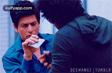 a man is holding a piece of paper in his mouth while another man looks on .