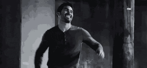 a man with a beard is smiling in a black and white photo while standing next to a pole .