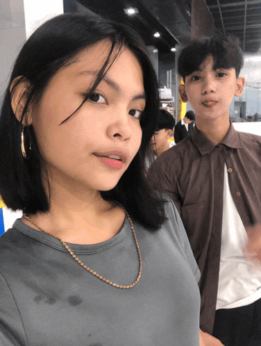 a girl wearing hoop earrings stands next to a boy wearing a brown shirt