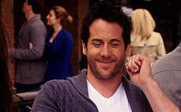 a man wearing a gray sweater and a white shirt smiles