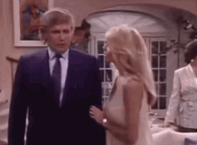 a man in a suit and tie is talking to a woman in a white dress in a living room .