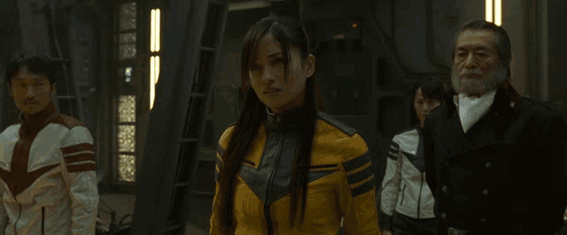a woman in a yellow jacket is standing in a room with other people