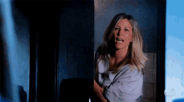 a woman in a white shirt is standing in a dark room and smiling