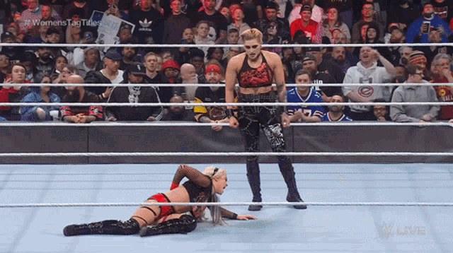 a female wrestler is laying on the ground while a man stands behind her in a wrestling ring