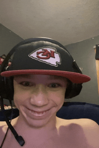 a young man wearing a chiefs hat and headphones smiles for the camera
