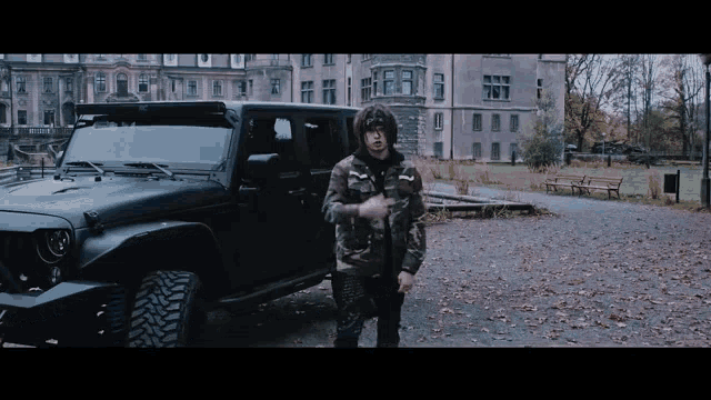 a man in a camo jacket stands in front of a jeep