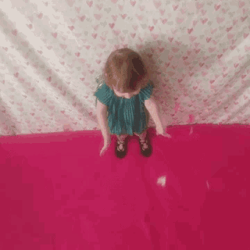 a little girl in a blue dress stands on a pink blanket with hearts on it