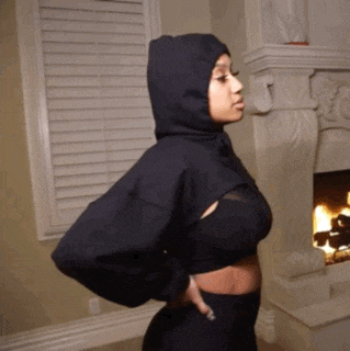 a woman wearing a black hoodie is standing in front of a fireplace in a living room .