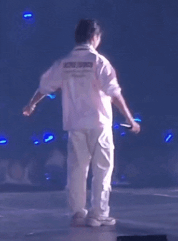 a man in a pink shirt and white pants is standing on a stage with a microphone .