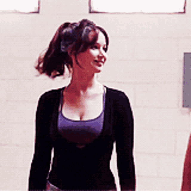a woman with a ponytail is wearing a black sweater and a purple top