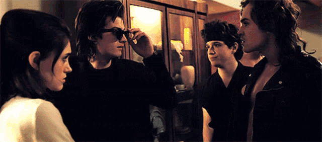 a man adjusts his sunglasses while standing next to a woman