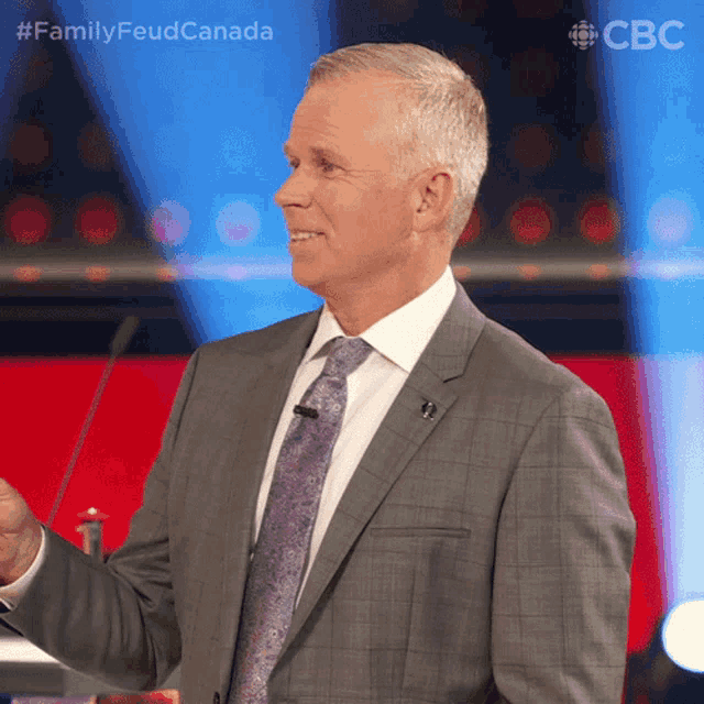 a man in a suit and tie is standing in front of a microphone with the hashtag familyfeud canada