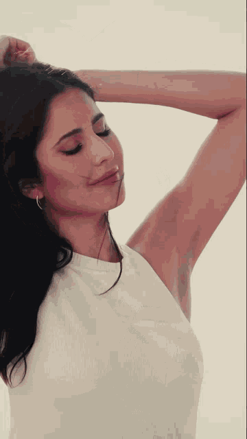 a woman in a white tank top holds her hair up in the air