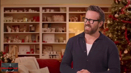 a man with glasses and a beard is standing in front of a christmas tree