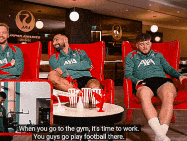 two men sit in red chairs in front of a sign that says jal japan airlines lounge