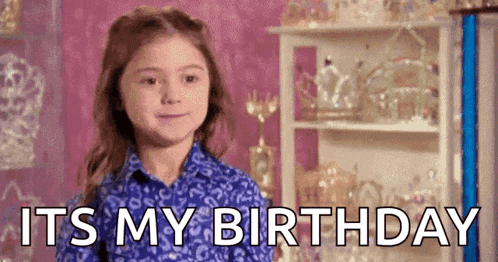 a little girl in a blue shirt is standing in front of a pink wall and says `` it 's my birthday '' .