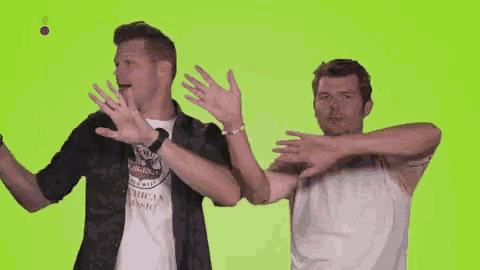 two men are dancing with their hands in the air on a green screen .