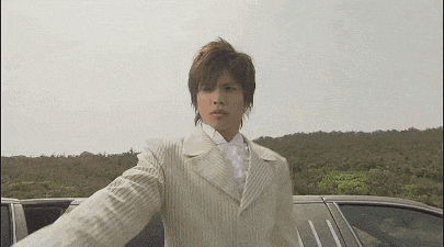 a man in a white suit and white tie is standing next to a car .