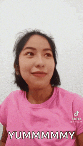 a woman in a pink shirt is making a funny face and saying yummmmy