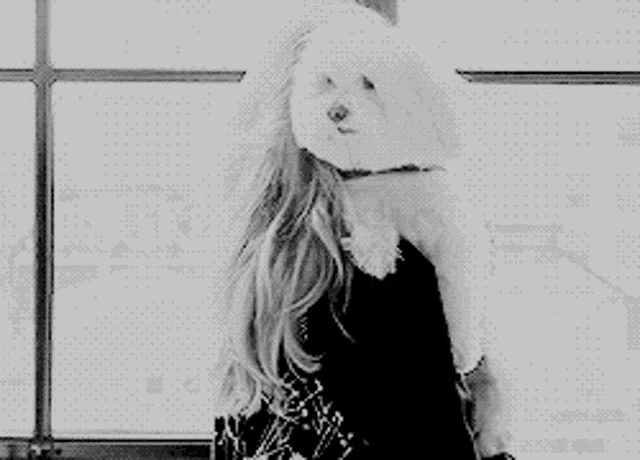 a woman is holding a small white dog in her arms in a black and white photo .