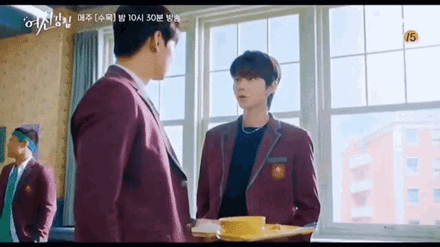 two men in school uniforms are standing next to each other in front of a window in a room .