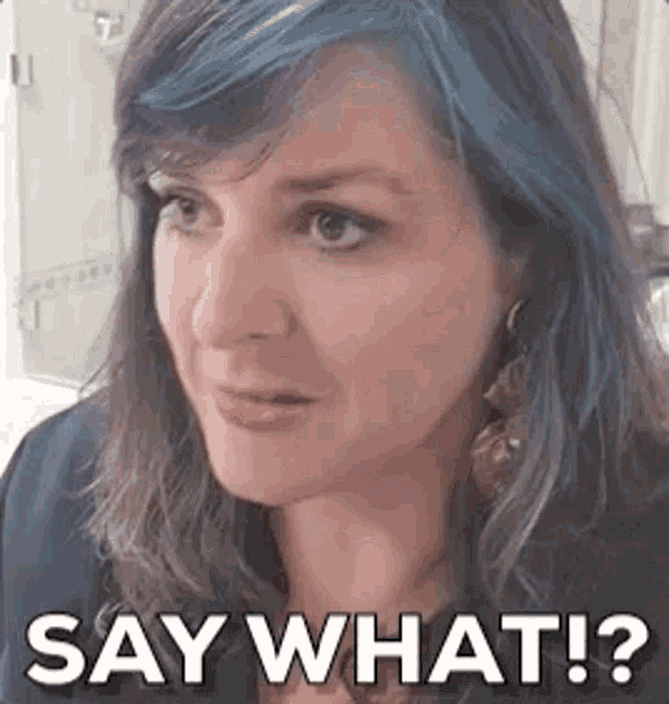 a woman with purple and blue hair is making a funny face and saying `` say what ? ''